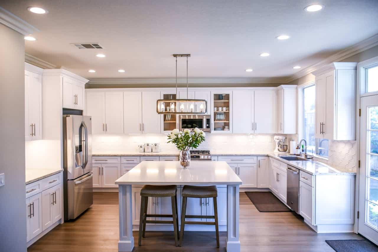 who-we-are Spacious and elegant kitchen featuring white cabinetry, island, and stainless steel appliances.