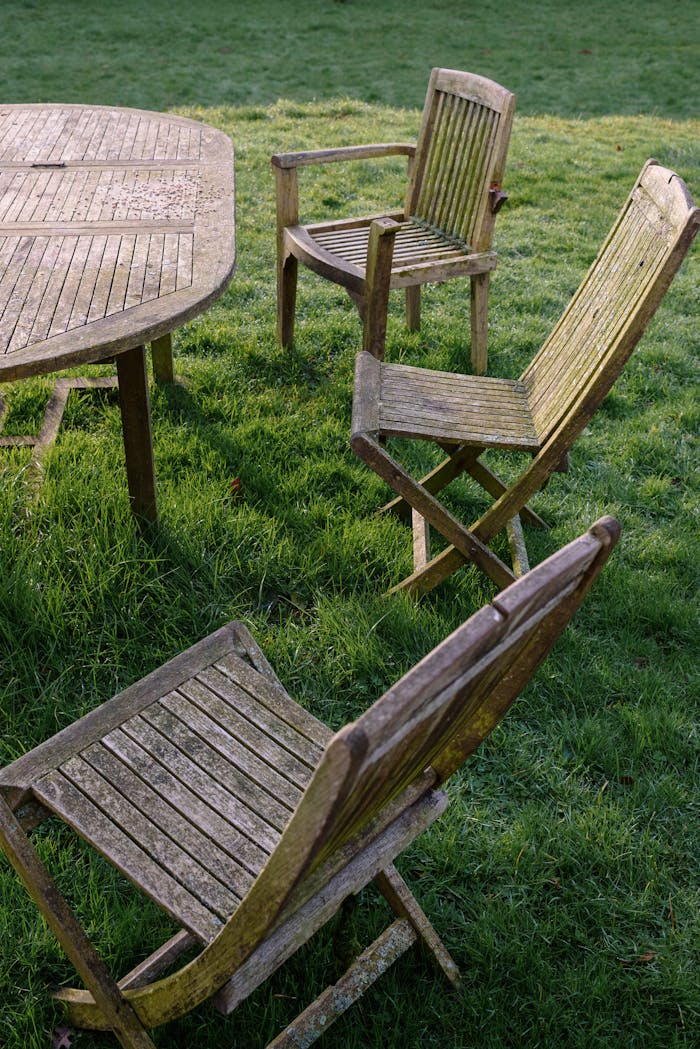 services-02 A set of weathered wooden chairs and table on a grassy lawn, conveying rustic charm.