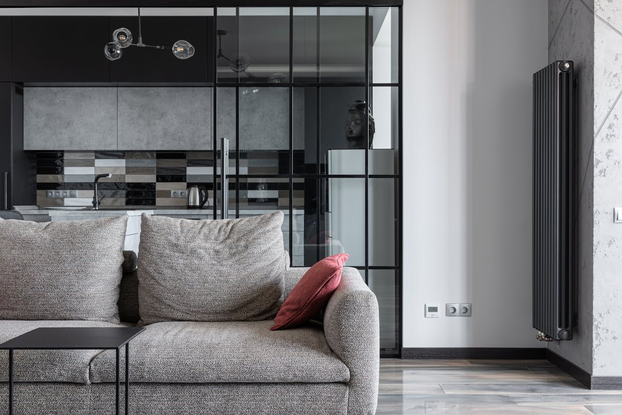 services-01 Contemporary living space featuring a stylish gray sofa, red cushion, and a view into a modern kitchen.